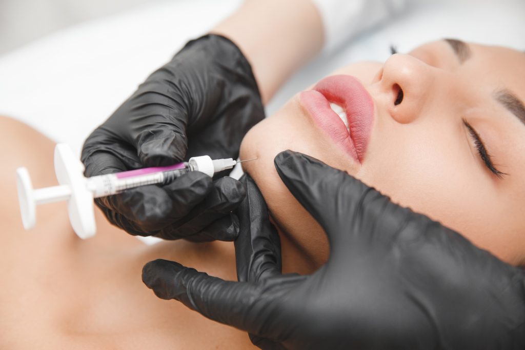 A cosmetologist makes lipolytic injections to burn fat on a woman's chin against a double chin.
