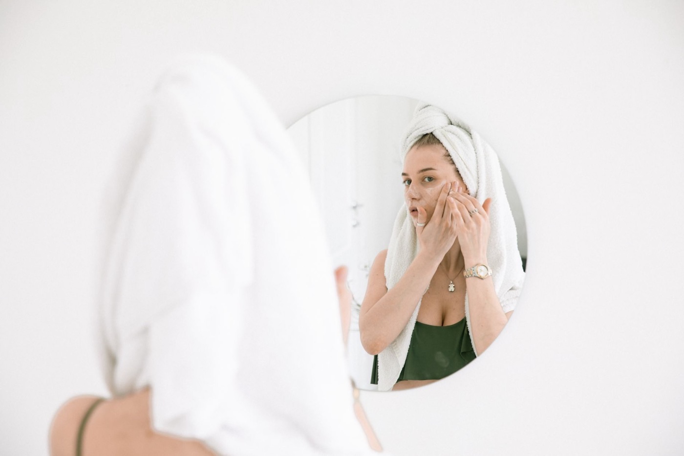 Mujer aplicándose crema hidratante en la cara frente al espejo